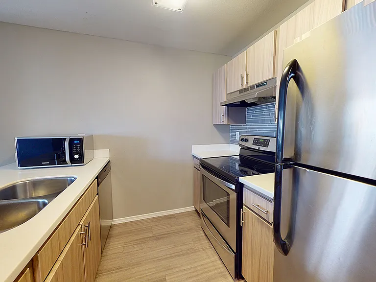 Apartment kitchen with stainless steel appliances, quartz countertops and wood-style flooring.
