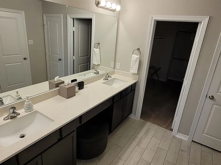 Primary bathroom with double sinks and vanity stool. Large walk-in closet