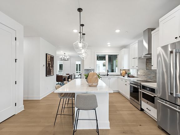 A modern, open-concept kitchen with a large white island, stainless steel appliances, and pendant li