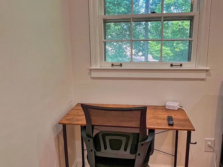 Dedicated work nook with a desk and chair, set beneath a large window with leafy views and hardwood flooring.