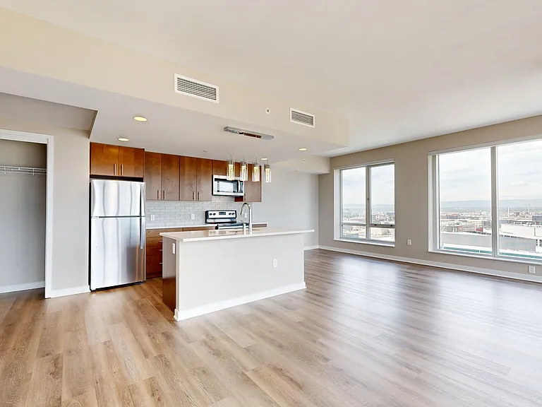 Apartment kitchen with stainless steel appliances, dining and living room with wood-style flooring.