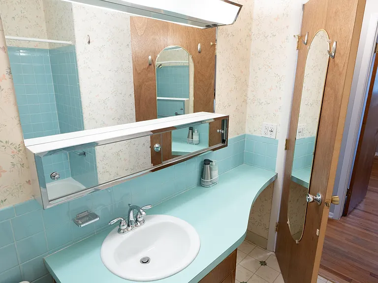 Original 1964 bathroom with period teal tabletop and tile. Through the door we see across the hallway into the east bedroom.