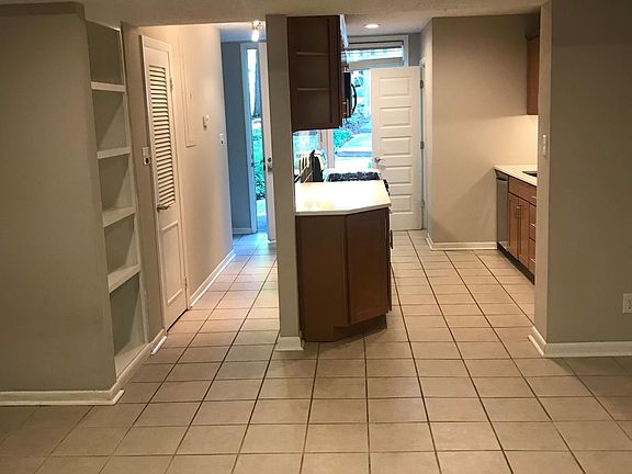 View from living room towards front hall entrance with built in bookcase, chef's kitchen, and powder room in the background.