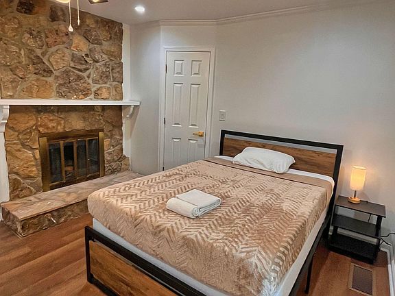 Private bedroom with a full-size bed, bedside table, and ceiling fan, plus a stone fireplace feature and wood floors.