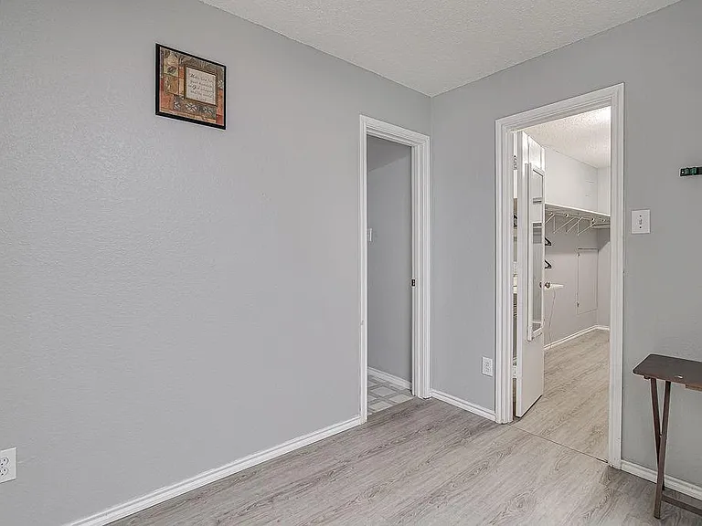 Spacious room with neutral walls, durable wood-look flooring, and easy access to an adjacent closet area.