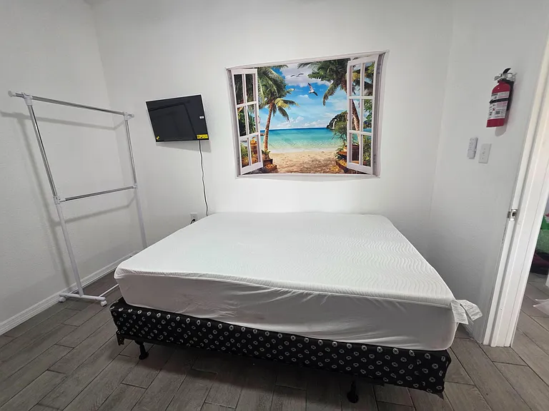 Private bedroom with tile flooring, wall-mounted TV, and space for a bed plus a freestanding clothing rack.