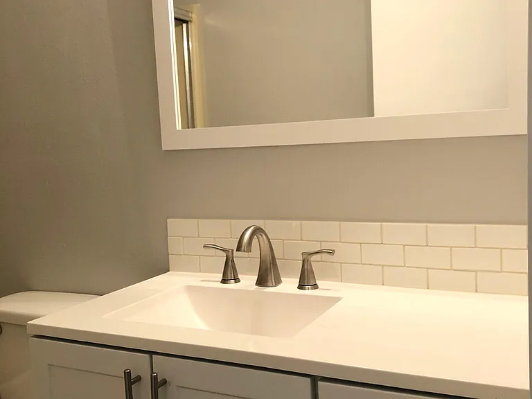 Newly renovated bathroom sink, vanity, mirror, and toilet .