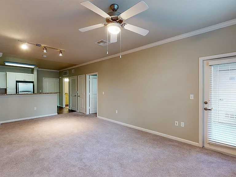 Apartment kitchen with stainless steel appliances, dining and living room with plush carpet flooring.