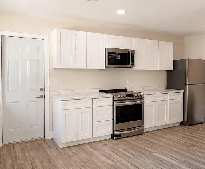 Galley-style kitchen with ample white cabinetry, marble-look counters, and stainless steel range, microwave, and fridge.