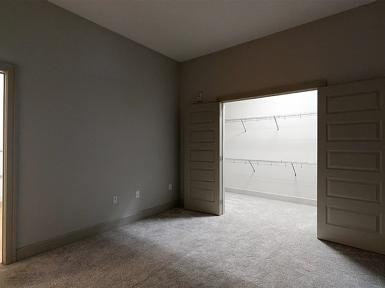 Spacious apartment bedroom with large closet, attached bathroom and plush carpet flooring.