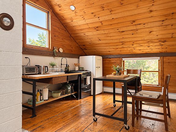 A charming, fully equipped kitchen featuring a retro SMEG refrigerator, butcher-block countertops, and an intimate dining area beneath vaulted wood ceilings.