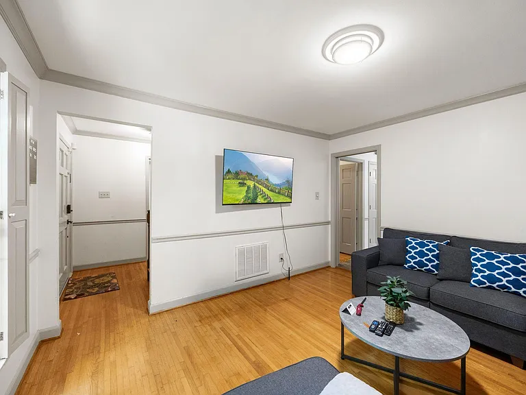Shared living room with hardwood floors, wall-mounted TV, and comfortable sectional seating with easy access to nearby rooms.