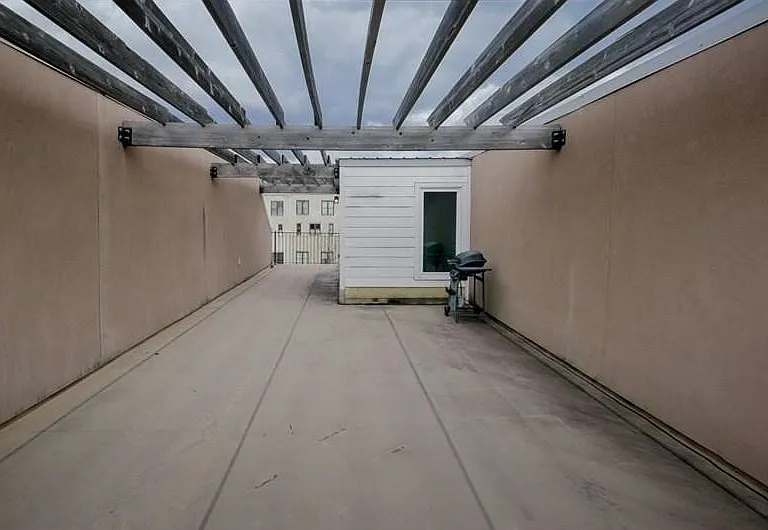 Expansive rooftop patio featuring a wooden pergola structure, stucco privacy walls, and concrete flooring