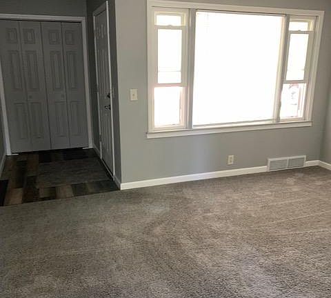 Living room w/ large front window with custom made mini blinds. Front door & coat closet can be seen to the left
