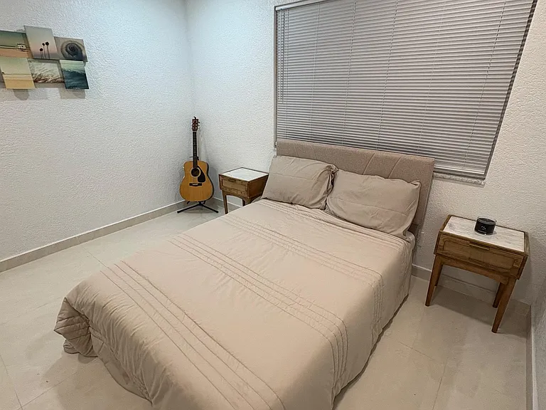 Furnished bedroom with a full bed, two nightstands, ceiling fan, and a wide window with blinds for easy light control.