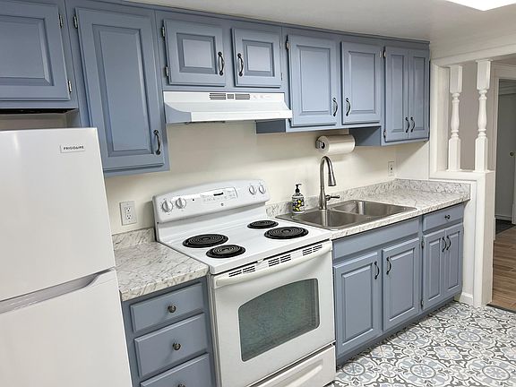 Brightly lit kitchen with new fridge, sink, freshly renovated solid wood cabinetry, and porcelain floor. New stove hood vents to the outside.
