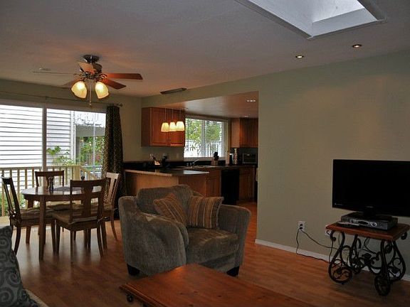 Continuing on, you see a better view of slider which opens to one of two decks and fully fenced side yard. Notice skylight above for lots of natural light, and open floor plan kitchen with plenty of lighting. Ceiling fans abound in the home for fresh air circulation.