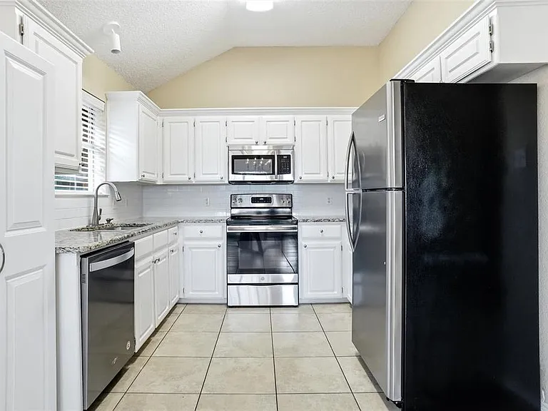 Kitchen featuring white cabinetry, granite countertops, tile flooring, stainless steel appliances, and a vaulted ceiling