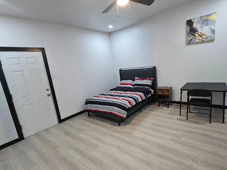 Furnished large private bedroom 3 with ceiling fan, bedside table, and a compact work desk, and access to balcony.