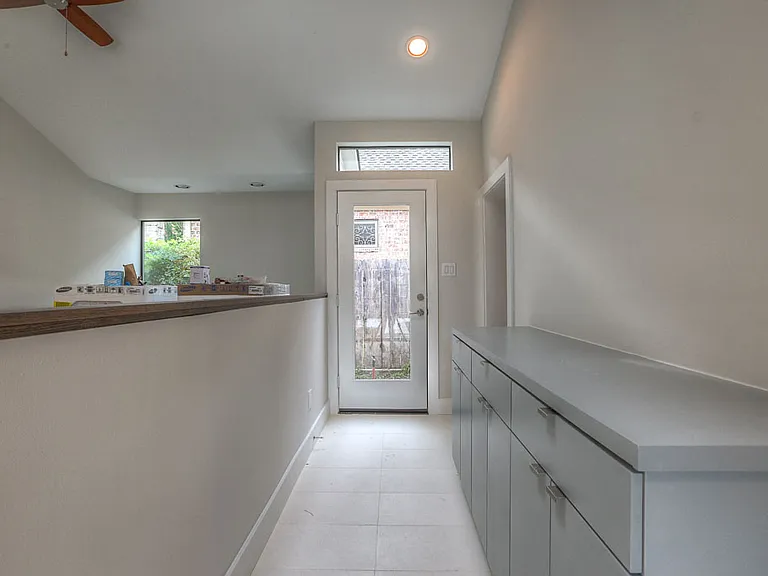 Mudroom/laundry corridor with tile floor, built-in gray base cabinets, exterior glass door to the sideyard, and a pass-through to the utility area