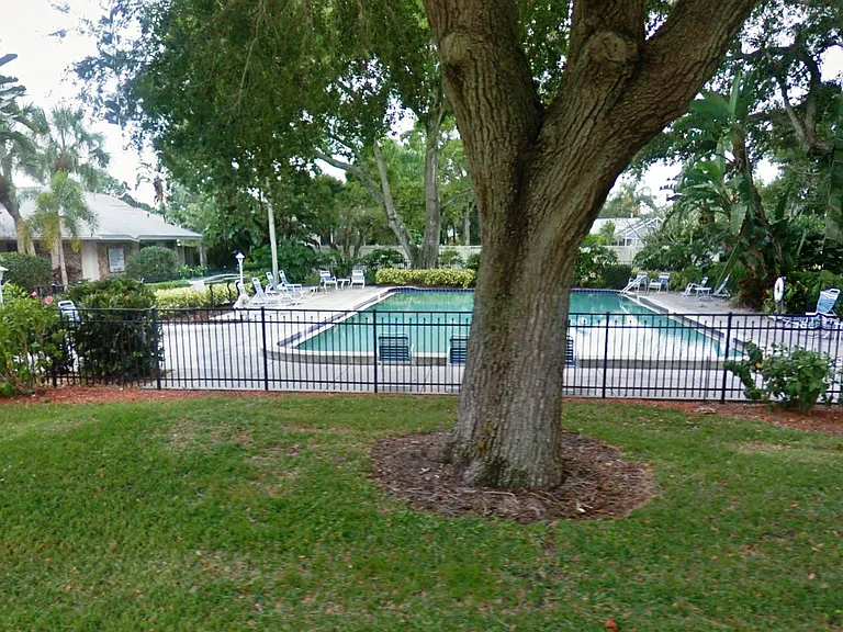 View of large pool next to community club house. Gated fence surrounds pool.