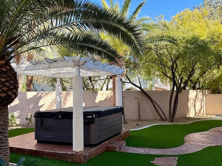 Backyard hot tub area with pergola-style cover and landscaped surrounding