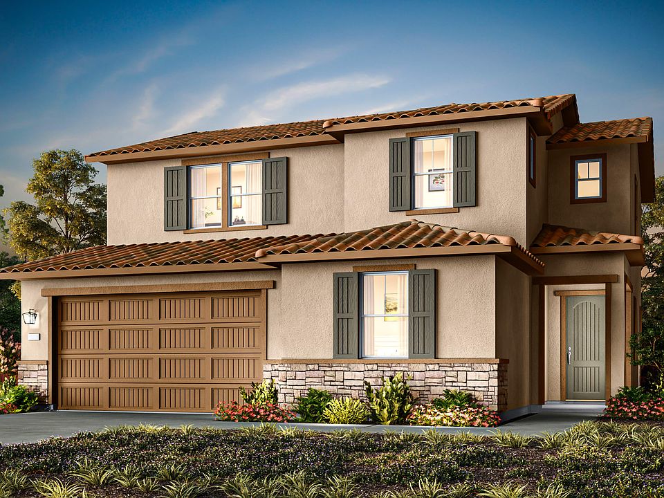 A two-story Mediterranean-style house with a tiled roof, stone accents, and a landscaped front yard