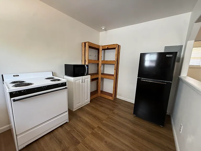 opposite view of kitchen w/microwave on cabinet, pantry shelves, fridge, in-unit circuit breaker panel and large open pass-through to front room