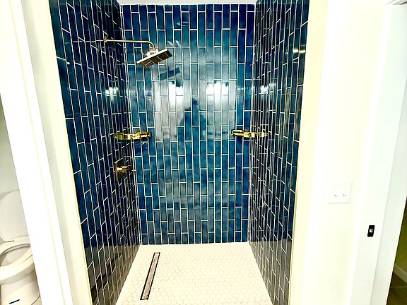 Primary site built shower with tile floor to ceiling, rectangular drain, gold finishes, rainfall shower head