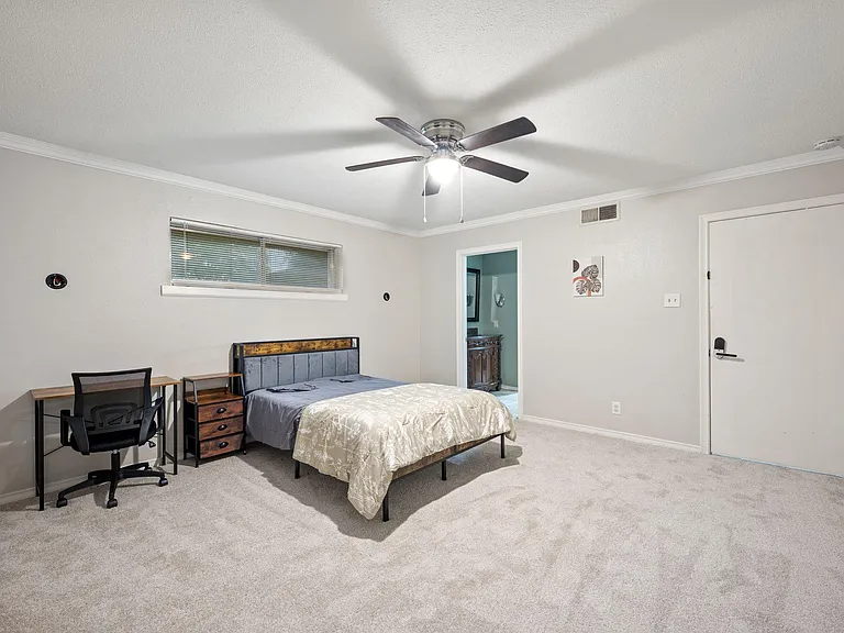 Spacious bedroom with ceiling fan, desk workspace, and convenient access to an en-suite bath and private entry.