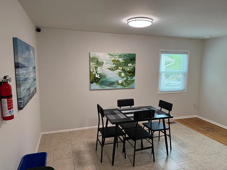 Dedicated dining area with a four-seat table, tile flooring, wall art accents, and a window with blinds for natural light.