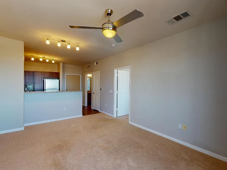 Apartment kitchen, dining and living room with plush carpet flooring.