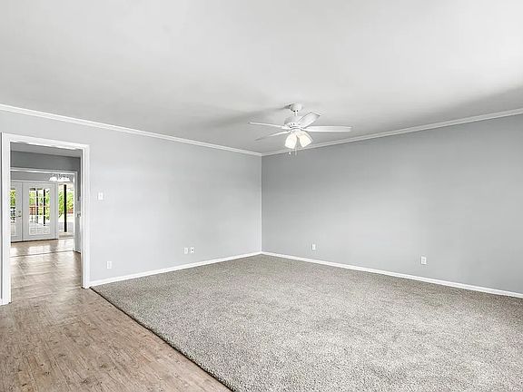 Living Room with new gray carpet, ceiling fan, and fresh gray paint, view into Kitchen, Dining Room, and Back Yard.