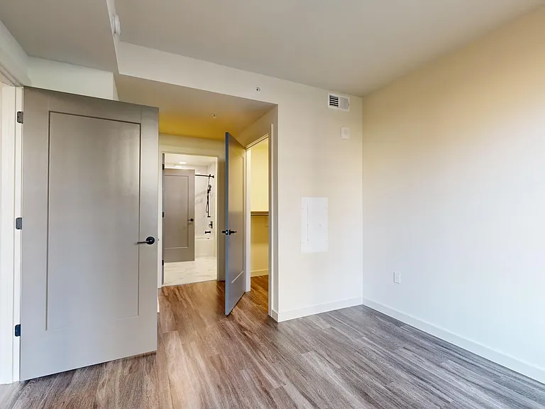 Spacious apartment bedroom with large closet, attached bathroom, and wood-style flooring.