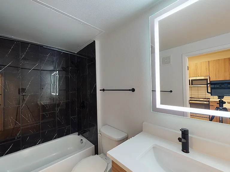Apartment bathroom with large soaking tub, wood-style flooring and LED vanity mirror.