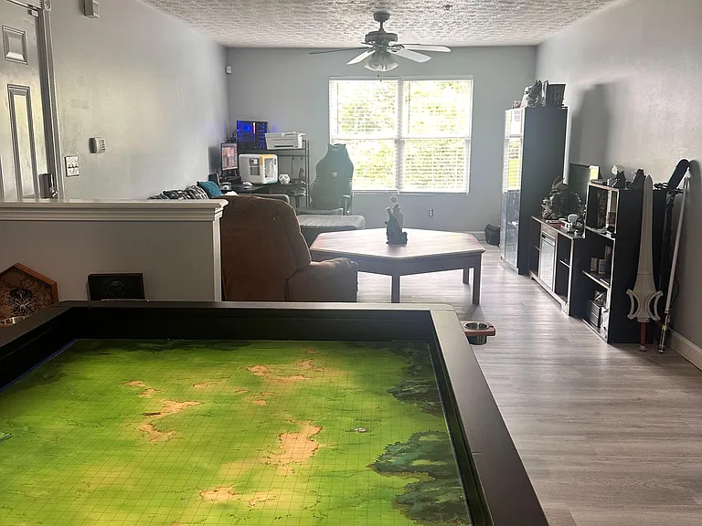 Open living area with a large window, ceiling fan, and flexible layout for seating, work, and game space.