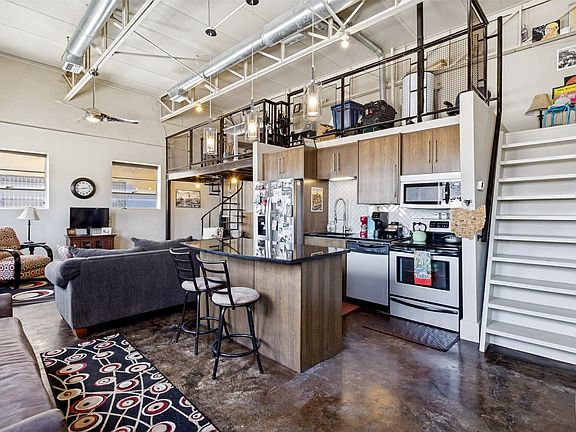 Open-concept living space featuring a lofted area with a spiral staircase, exposed ductwork, wood-finish cabinetry, a kitchen island with a dark countertop, and polished concrete flooring
