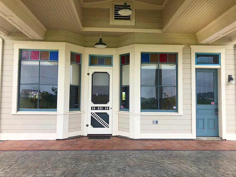 The beautiful covered carport with storefront stained glass windows, screen door and industrial porch lights is reminiscent of the Victorian era.