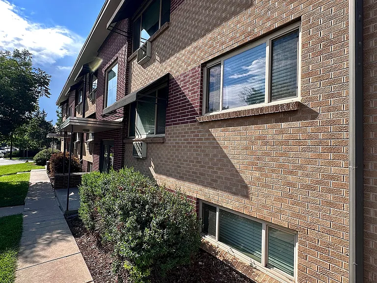 Charming brick apartment building with well-maintained landscaping and large windows, basking in beautiful sunlight.