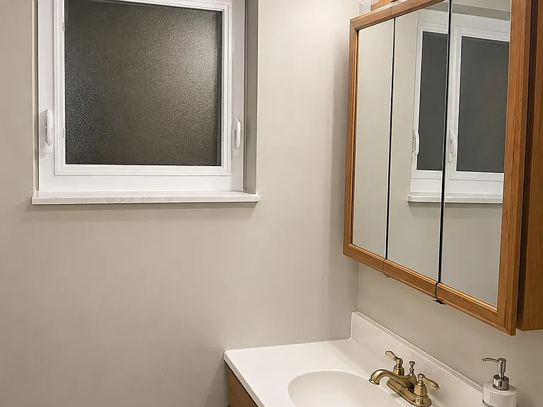 Updated vanity area with integrated sink, mirrored medicine cabinet, and frosted window for privacy and natural light.