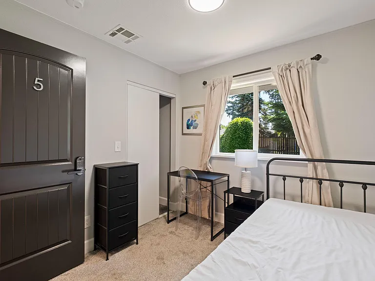 Furnished bedroom with a large window, desk workspace, and dresser storage, plus a sliding-door closet for easy organization.