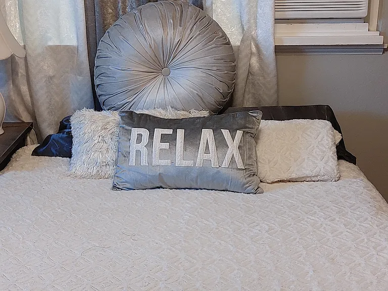 Queen bed with multiple decorative pillows, east facing wall, window a/c unit