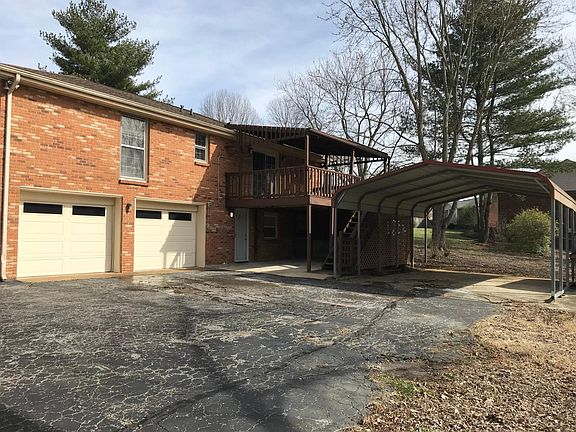 Back of the house with two car garage, covered patio/parking area and carport. Also has stairs leading up to covered deck.