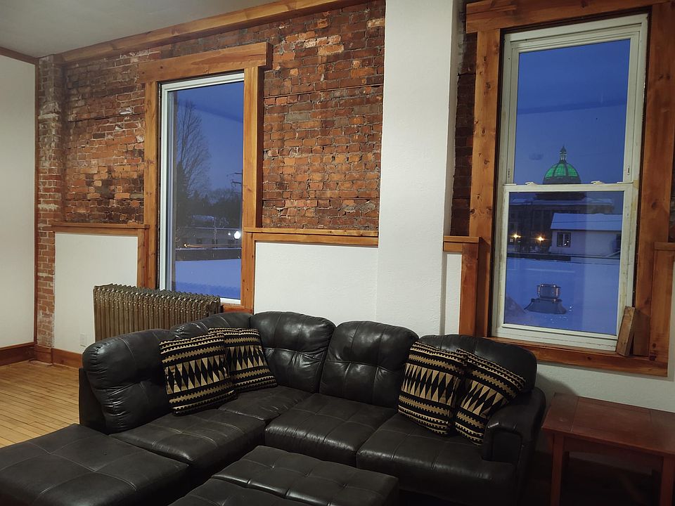 Beautifully remodeled living room with exposed brick walls, floor to ceiling windows, and refinished hardwood floors. Gorgeous views of Oneida County Courthouse. Leather sectional sofa.