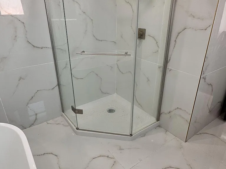 Spa-style bathroom features a glass corner shower with rainfall head, large-format tile, and recessed lighting.