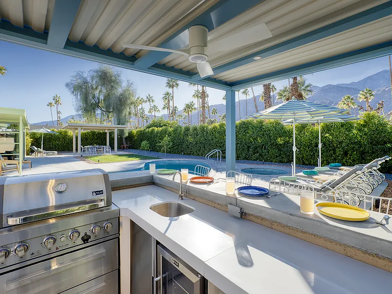 Outdoor kitchen with BBQ, fridge, sink and counter seating.