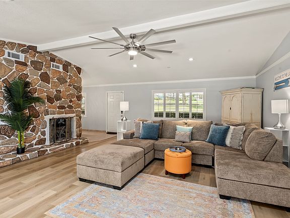 Vaulted ceiling, stone-clad fireplace, wood-finish flooring, recessed lighting, and a ceiling fan