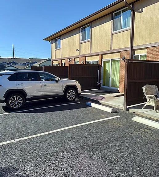 Inviting suburban apartment with convenient parking, featuring a modern vehicle in front of charming two-story brick and wood exterior.