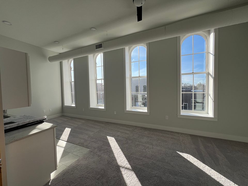 Living area with kitchen with windows facing west. All windows have shades.