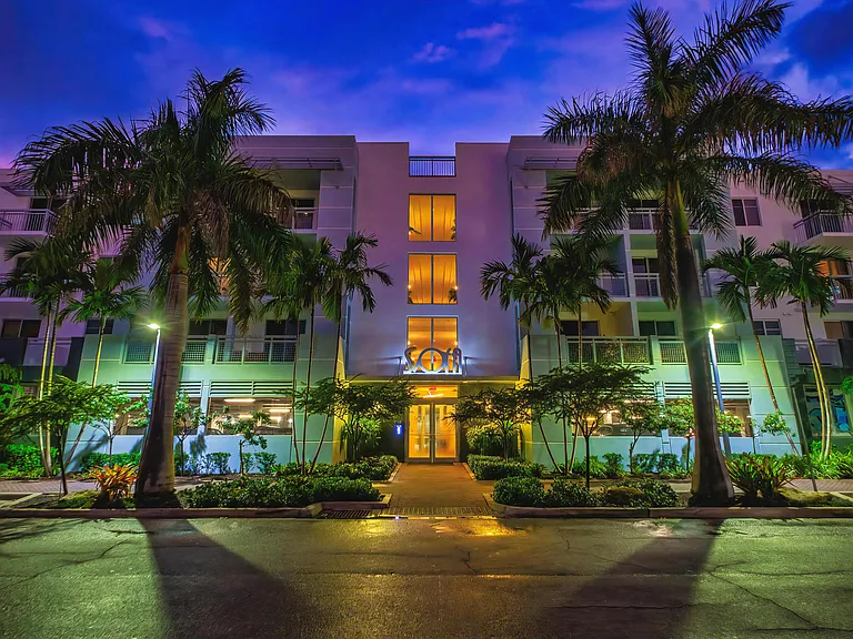 Exterior View of Apartment Building at Dusk Framed by Palm Trees and Lit Entry Path